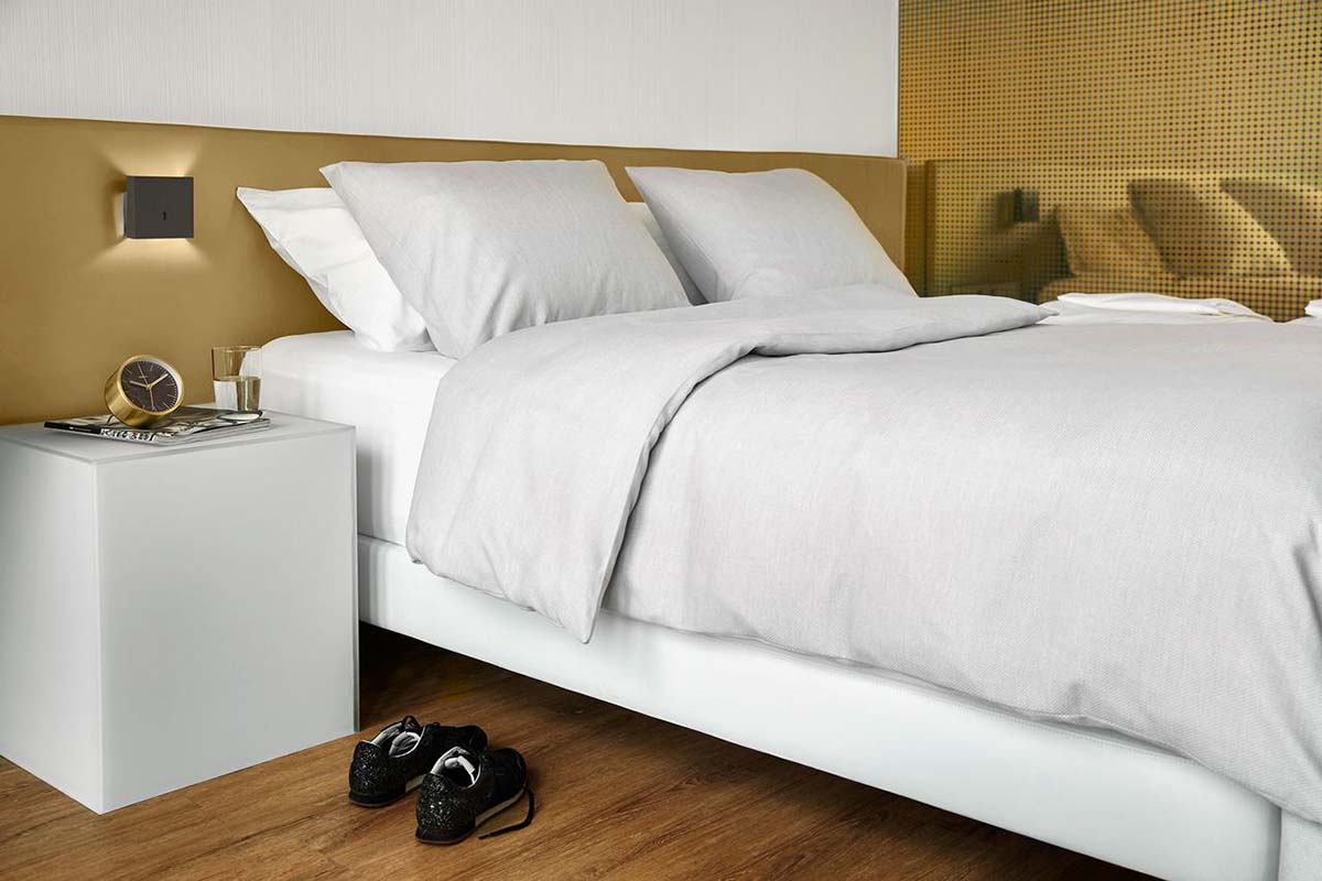 Hotelbed met wit beddengoed en grijze sprei van Blycolin