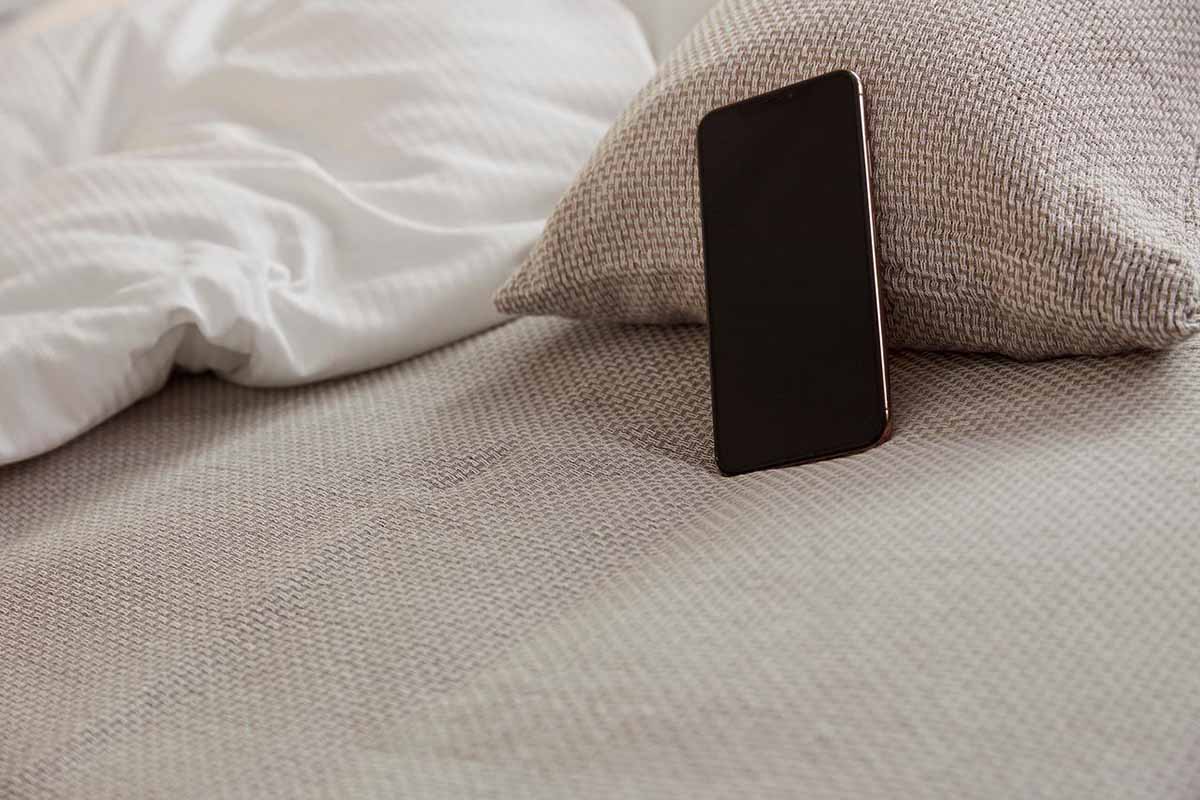 Close-up van een beige bedloper en kussen van Blycolin met een smartphone op het bed
