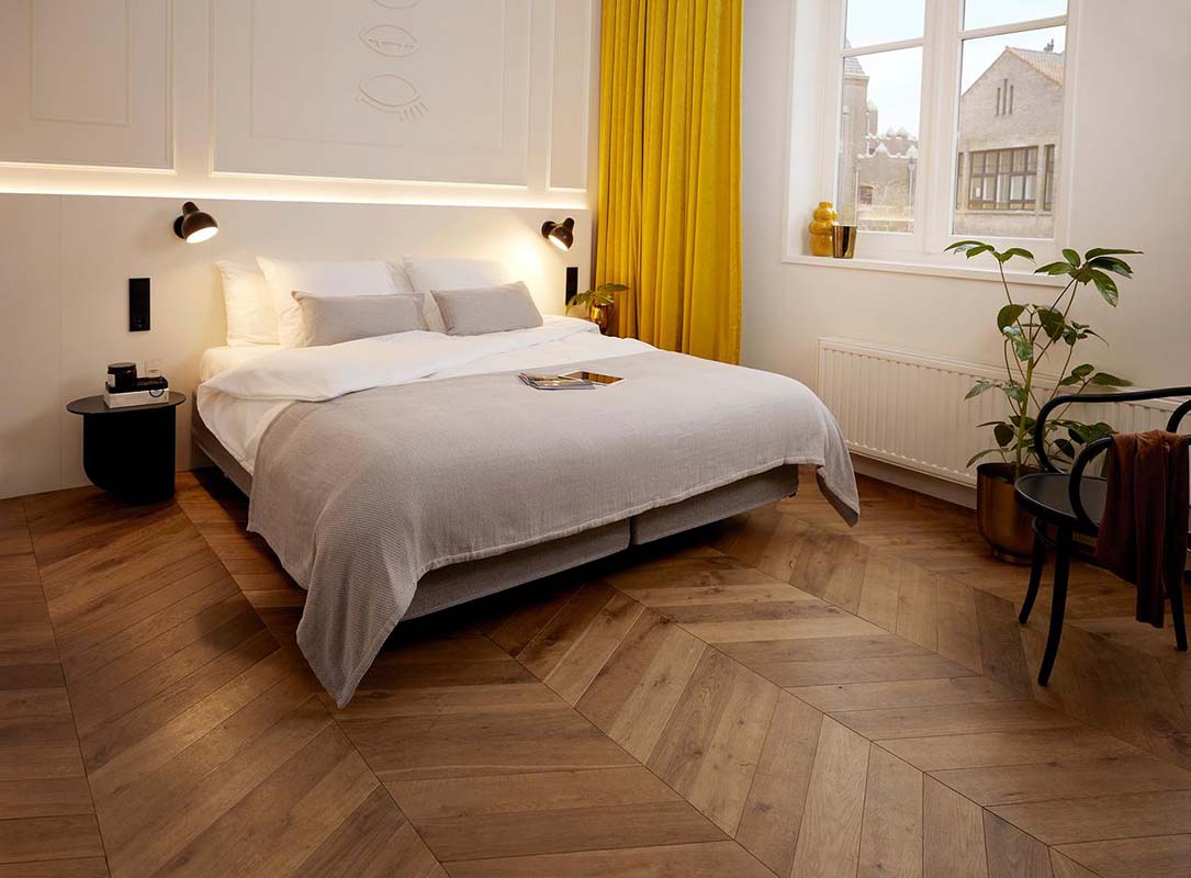 Hotelkamer met bed opgemaakt in wit linnen en een grijze bedloper