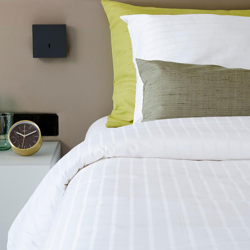 Bed met wit gestreept dekbedovertrek en groene kussens