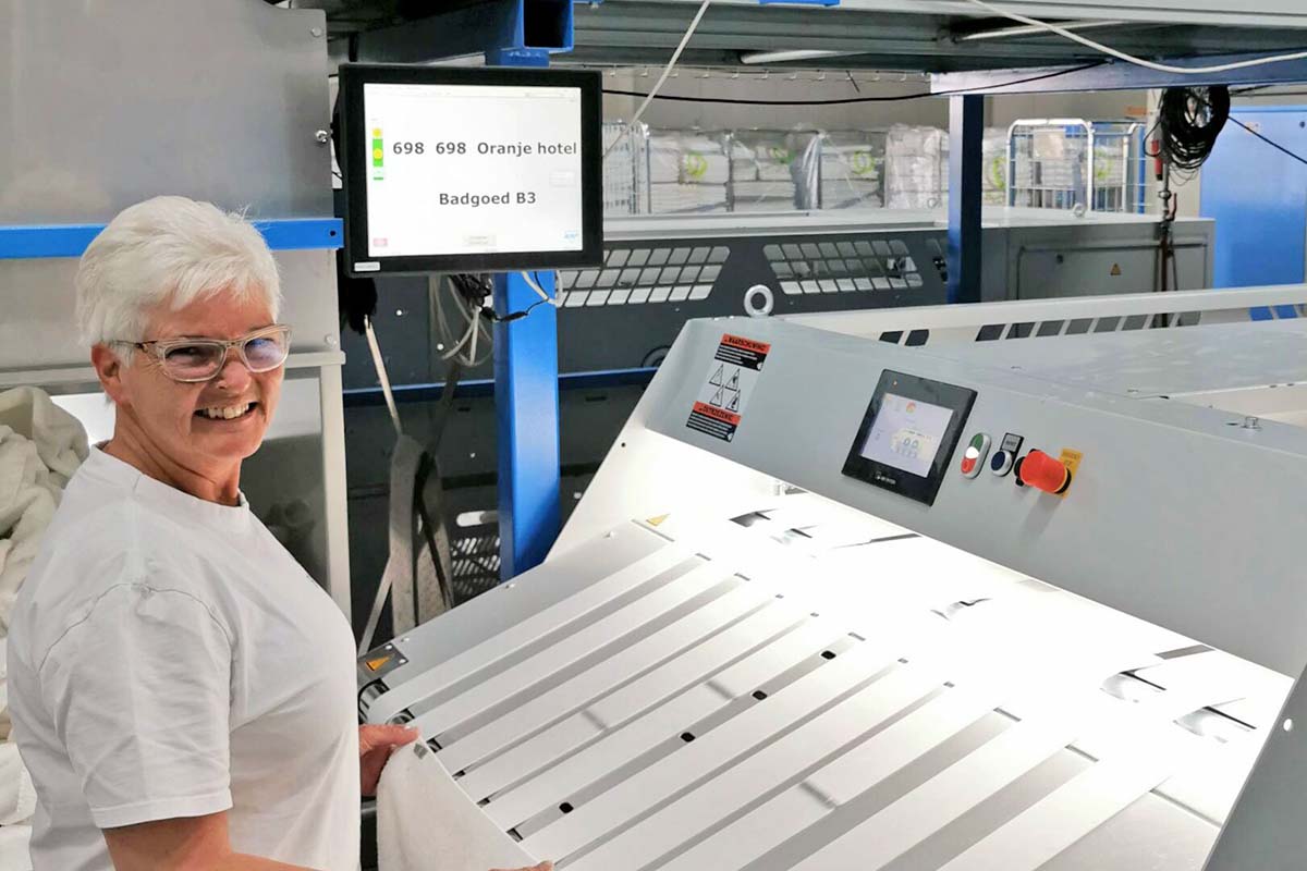 Rika lacht bij een vouwmachine in de wasserij van Blycolin