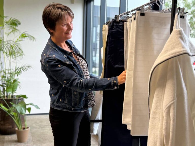 Medewerker van Blycolin bekijkt textiel uit de collectie aan een kledingrek